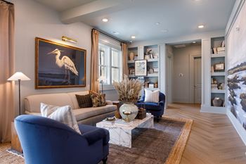 A living room with a blue chair and a painting of a white bird on the wall.